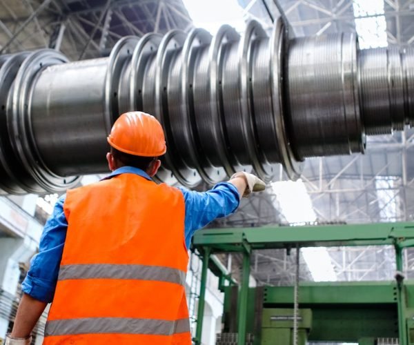 Engineer in high visibility vest and hard hat inspecting large machinery in factory setting.