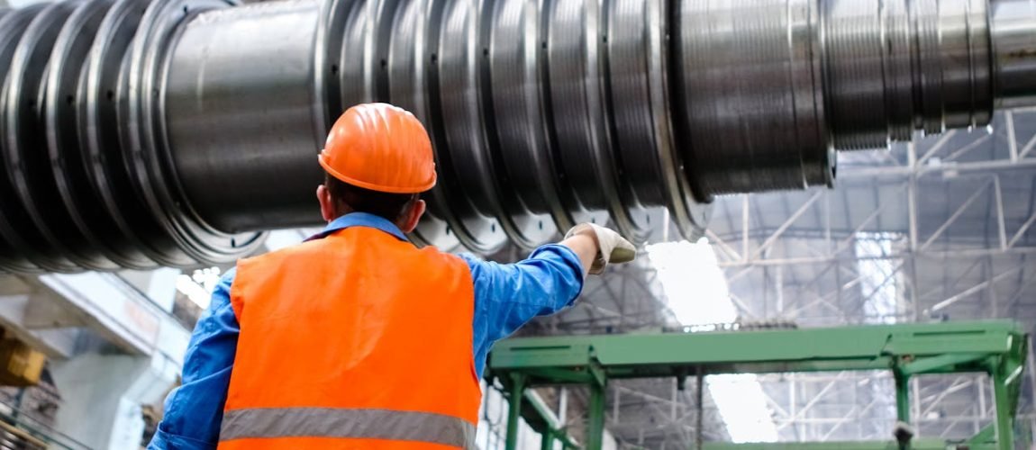 Engineer in high visibility vest and hard hat inspecting large machinery in factory setting.